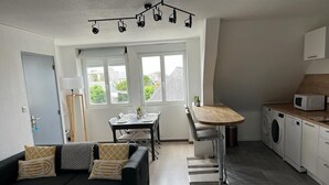 A compact living space with a sofa, dining table, and kitchen area including a washing machine.