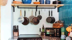 Cocina compacta con estufa, horno y microondas. Hay repisas superiores con utensilios y batería de cocina.
