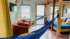 Una hamaca en una habitación con una cama de madera, un sofá marrón y un televisor en la pared.