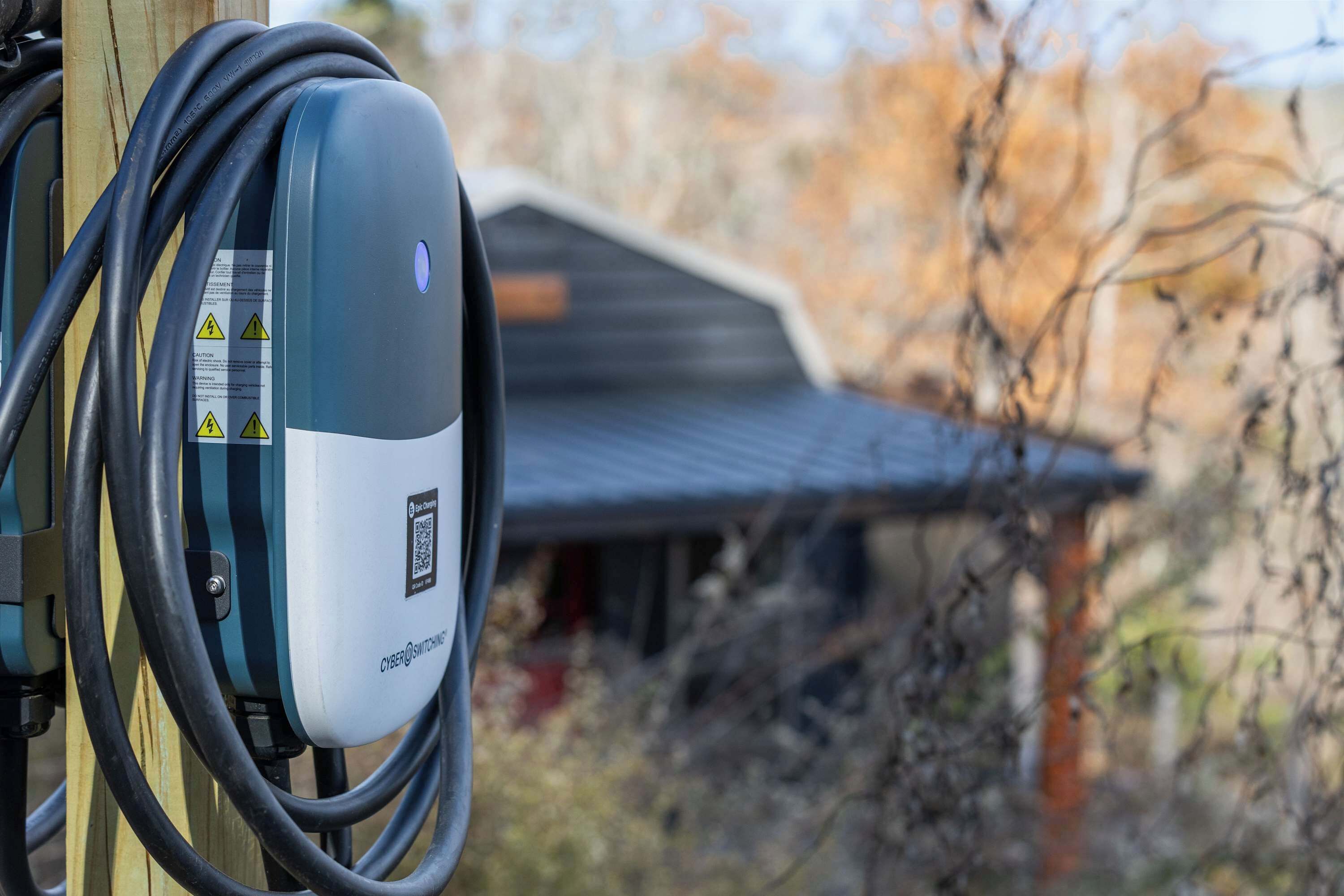 An electric vehicle charging station with a QR code and warning labels, connected to a cable.