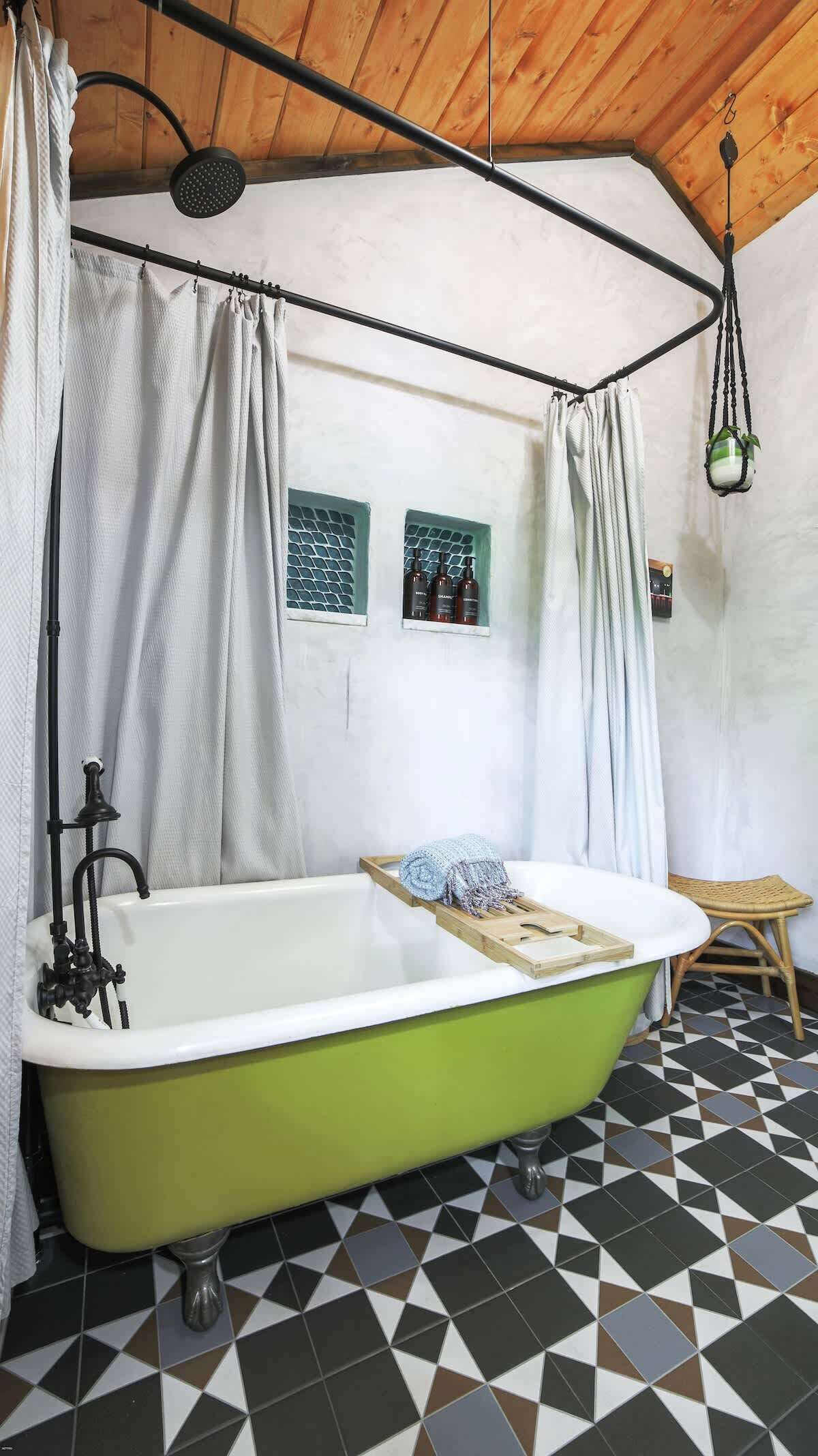 A bathroom with a green bathtub, white curtains, a showerhead, a small window, and a hanging plant.