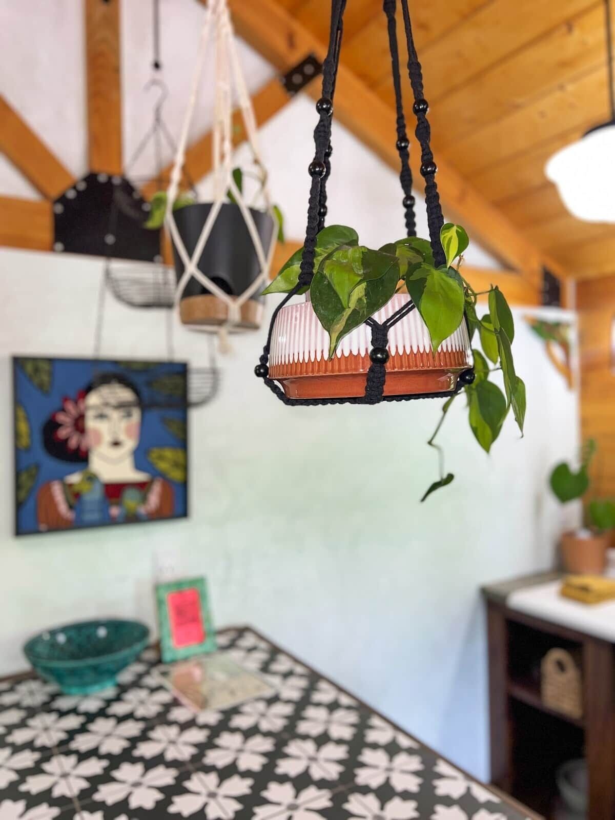 A hanging plant in a terracotta pot, a decorative wall hanging, and a patterned tablecloth.