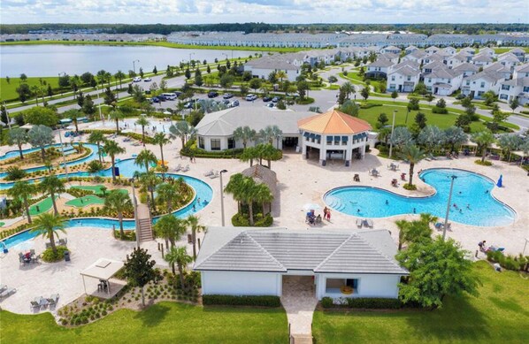 A resort with multiple swimming pools, a central building, and a view of a lake.