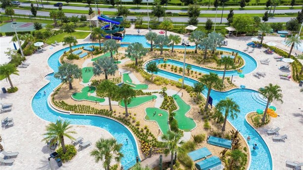 Une grande piscine extérieure dotée de plusieurs couloirs de nage et d’un toboggan, entourée de palmiers et de chaises longues.