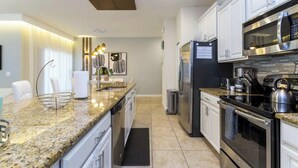 Une cuisine moderne dotée de plans de travail en granit, d’appareils électroménagers en acier inoxydable et de meubles blancs.