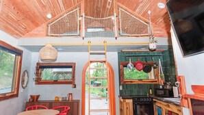 A rustic interior with a wooden ceiling, a kitchen with hanging pots, and a dining area with red chairs. - Whippoorwill: Cozy Mountain Escape w/ Stargazing Shower & Trails (Marion County)