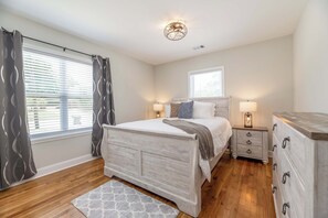 Un dormitorio con una cama de madera, mesitas de noche con lámparas, un aparador y una ventana con cortinas.