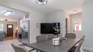 Eine moderne Küche mit integriertem Kühlschrank, einem Essbereich mit langem Tisch und Korbstühlen sowie einem an der Wand montierten Flachbildfernseher.