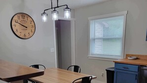 Ein Essbereich mit Holztisch und Stühlen, einer Wanduhr und einem Fenster mit Jalousien.