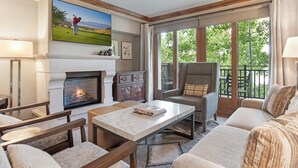 A cozy living room with a fireplace, comfortable seating, a television, and large windows offering a view of the outdoors. - 2 BR 2 BA Unit in Vail Village Beautiful Sebastian Residence w 5 Star Amenities (Vail)