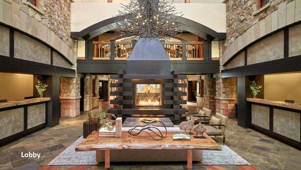 A lobby with a central fireplace, stone walls, and a wooden reception desk. - 2 BR 2 BA Unit in Vail Village Beautiful Sebastian Residence w 5 Star Amenities (Vail)