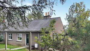 Una casa in pietra con tetto grigio, un camino e un muro di pietra di fronte.