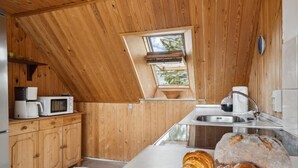 Une cuisine compacte aux murs en bois, dotée d’un puits de lumière, d’un four à micro-ondes, d’une machine à café, d’un évier et d’une miche de pain.