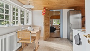Une cuisine compacte dotée d’un réfrigérateur intégré, un coin repas avec une table et des chaises, et une fenêtre donnant sur un espace verdoyant.