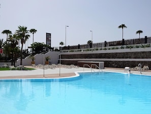 A swimming pool with lounge chairs, palm trees, and a stone wall. - Holiday Vibes in Playa del Inglés (Playa del Inglés)