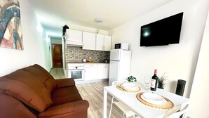 Ein modernes Wohnzimmer mit einem braunen Sofa, einem Esstisch mit weißen Stühlen und einer Küche im Hintergrund.