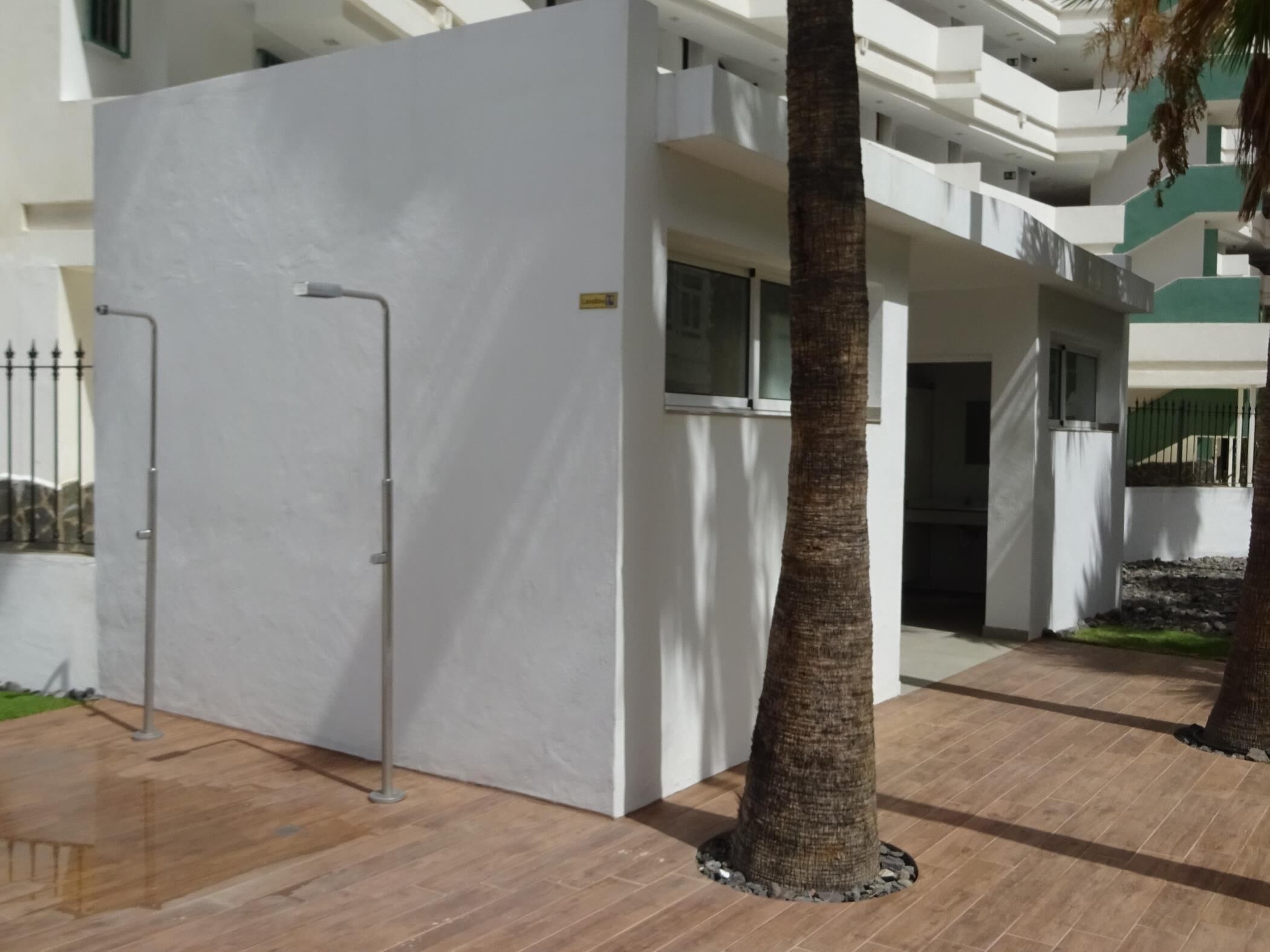 Un edificio moderno con fachada blanca, una cerca de metal y una palmera en primer plano.