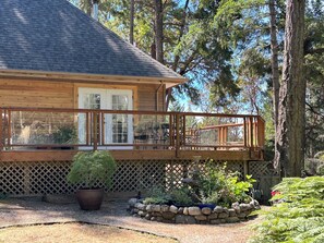 A wooden cabin with a balcony, surrounded by a garden with various plants and a stone wall. - woodland escape (saltspring island)