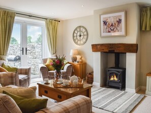 A cozy living room with a fireplace, a stone wall, and a large window with curtains.