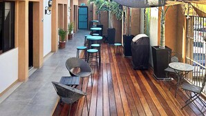 A covered outdoor patio with wooden flooring, several tables and chairs, and potted plants. - Dreamy Condo in Centro Histórico + Unlimited Pool Club Access! (Todos Santos)