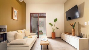 A modern living room with a sofa, a coffee table, a TV, and a potted plant. - Dreamy Condo in Centro Histórico + Unlimited Pool Club Access! (Todos Santos)