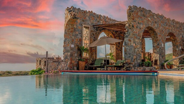 A stone structure with arches over a pool, surrounded by greenery and a sunset sky. - Dreamy Condo in Centro Histórico + Unlimited Pool Club Access! (Todos Santos)