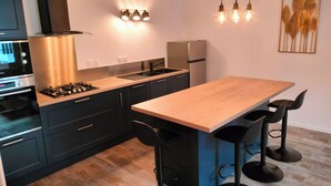 Una cocina moderna con una isla central, taburetes negros tipo barra, horno empotrado y refrigerador.