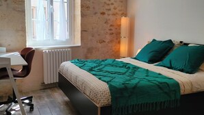 Un dormitorio con cama, escritorio, silla, ventana con cortinas y lámpara colgante.