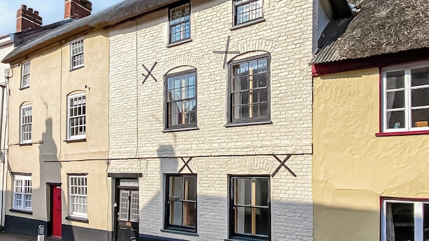 En traditionel bygning med mange vinduer og en røddoor, med facade af mursten og stråtækt tag.
