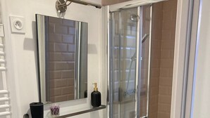 Un baño moderno con cabina de ducha de vidrio, un lavamanos blanco, un mueble de tocador negro y un espejo sobre el lavamanos.