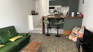 Una sala de estar con un sofá verde, un tapete estampado, una mesa de centro y un mueble para televisión con una pantalla plana.