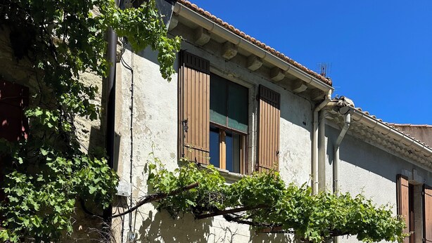 Un edificio rústico con fachada de piedra, contraventanas de madera y entrada cubierta de hiedra.