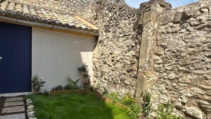 Muro de piedra junto a un edificio con una puerta azul y un pequeño jardín con césped y plantas.