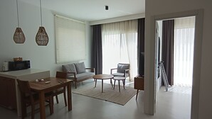 A modern living room with a sofa, two armchairs, a coffee table, and a dining area with a table and chairs. - Gizz Suites City (Fethiye)