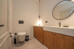 A modern bathroom with a toilet, a sink, a mirror, and wooden cabinets. - Gizz Suites City (Fethiye)