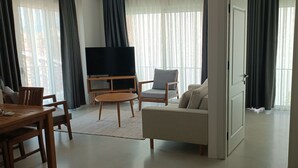 A modern living room with a flat-screen TV, a sofa, a chair, and a dining table. - Gizz Suites City (Fethiye)