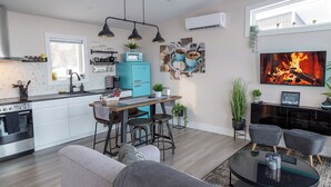 A modern kitchen with a central island, a dining area with bar stools, a living room with a fireplace, and a TV mounted above the fireplace. - Lake View Cottage with Private Hot Tub - Eagle View (West Bay)