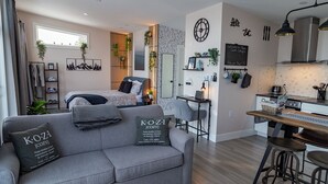 A modern apartment with a grey sofa, a bed, a kitchen area, and a dining table. - Lake View Cottage with Private Hot Tub - Eagle View (West Bay)