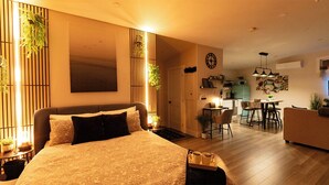 A modern bedroom with a large bed, bedside tables, and a nightstand. There is a dining area with a table and chairs, and a kitchen area with a refrigerator and cabinets. - Lake View Cottage with Private Hot Tub - Eagle View (West Bay)