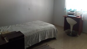 A small, sparsely furnished room with a bed, a desk with a printer, and a chair. - Casa para temporada  (Brasília)