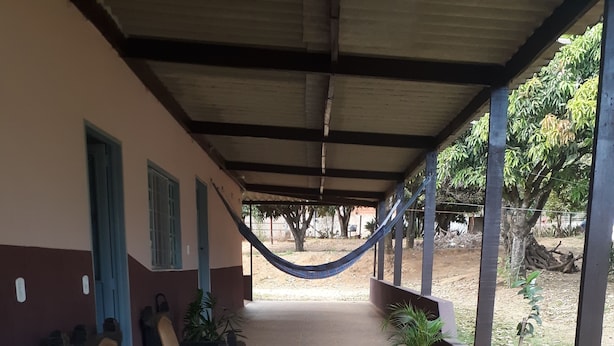 A covered outdoor seating area with stone flooring, benches, and potted plants. - Casa para temporada  (Brasília)
