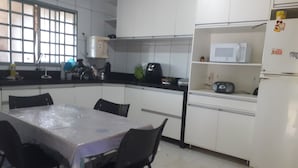 A kitchen with white cabinets, a dining table with chairs, a microwave, and a refrigerator. - Casa para temporada  (Brasília)