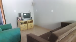 A living room with a brown sofa, a teal armchair, and a wooden cabinet with a television. - Casa para temporada  (Brasília)
