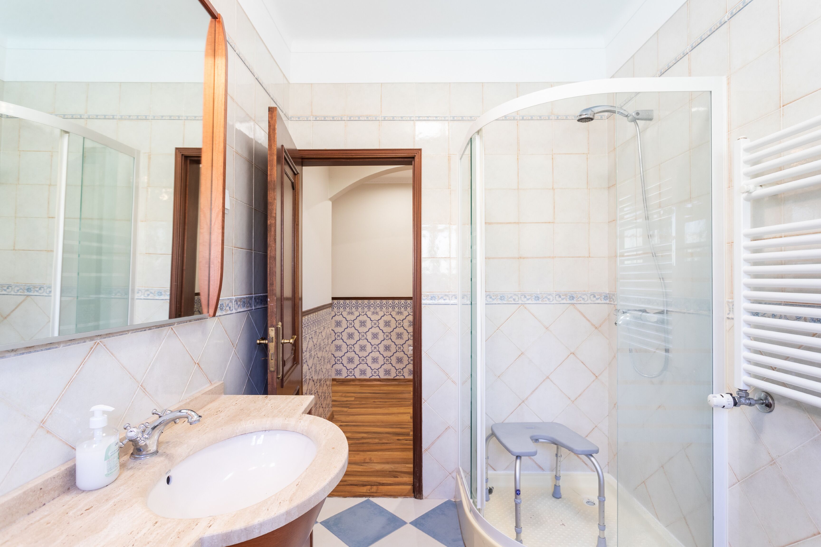 A bathroom with a sink, mirror, shower, and a small step stool.