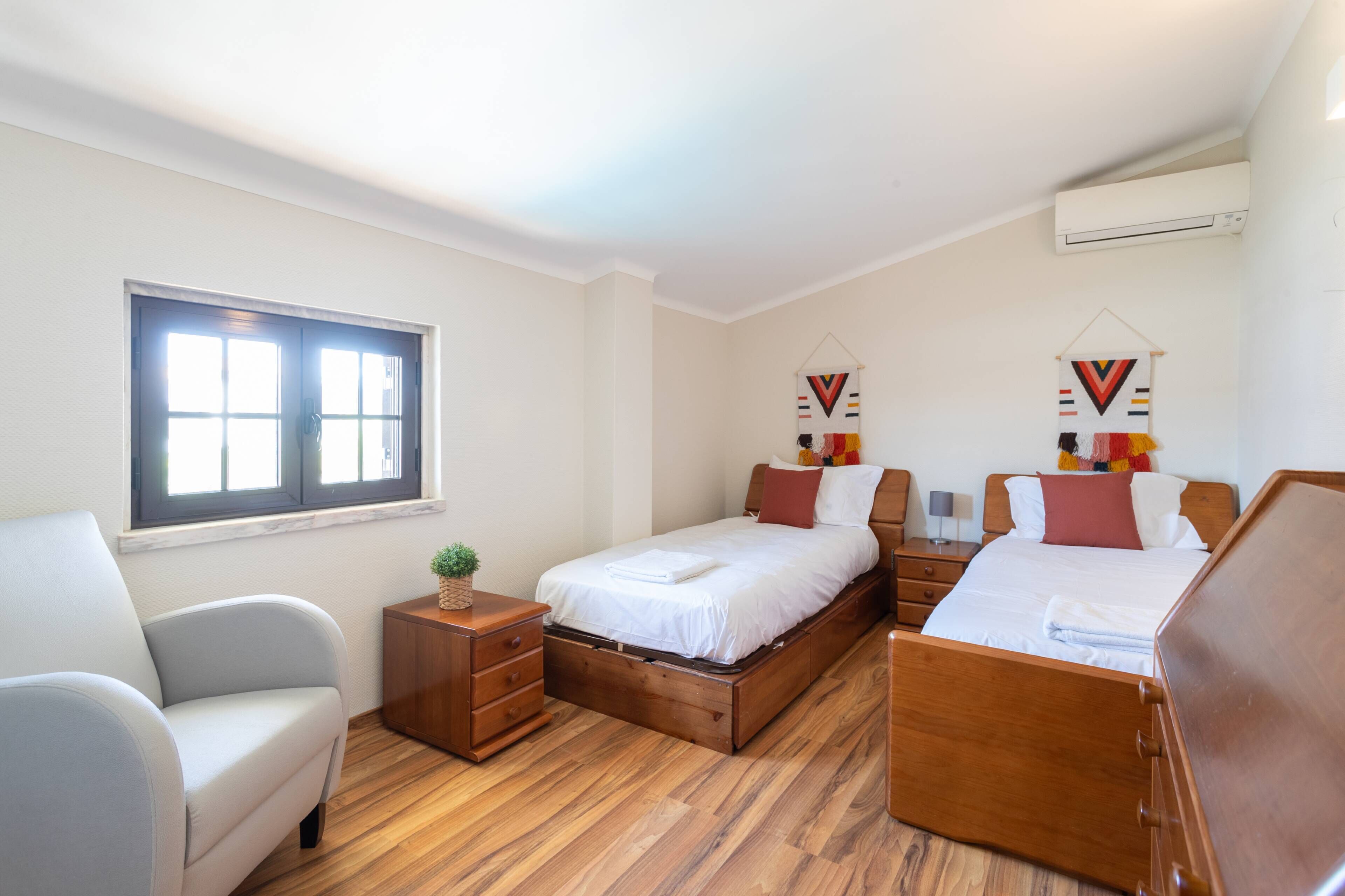 Un dormitorio con cama, una silla, una mesita de noche y una ventana.