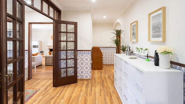 Un hall d’hôtel avec un plancher en bois, un comptoir d’accueil, un comptoir blanc et une porte donnant sur un espace de détente.