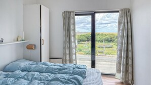 Ein Schlafzimmer mit Bett, Kleiderschrank und Blick auf einen Park durch eine Glastür.