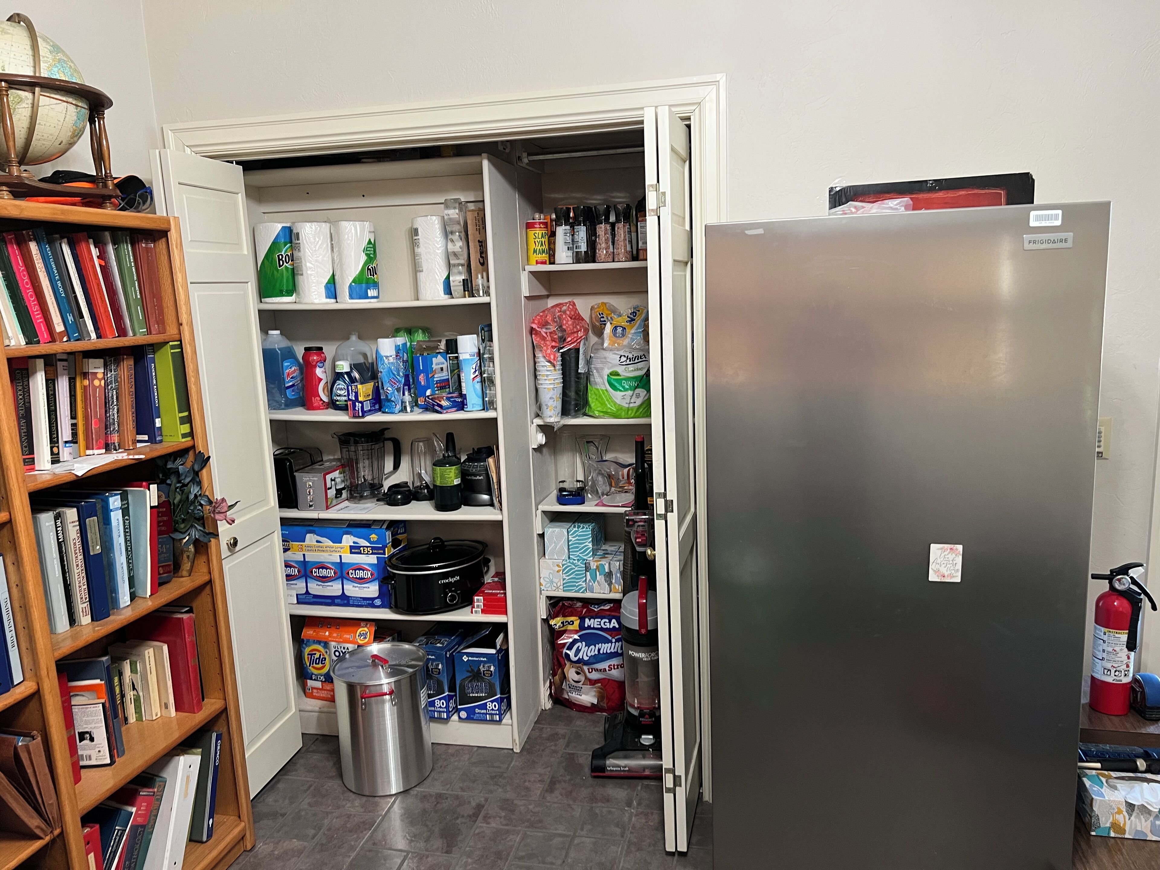 Une cuisine équipée d’un réfrigérateur, de rayonnages ouverts remplis de provisions, d’un évier et d’une bibliothèque remplie de livres.