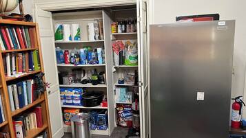 Une cuisine équipée d’un réfrigérateur, de rayonnages ouverts remplis de provisions, d’un évier et d’une bibliothèque remplie de livres.