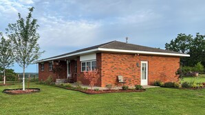 A single-story brick house with a front porch, a small garden, and a clear sky. - Ben Ranch House overlooking river - Full 3 Bedroom house. Minutes from Fairfax. (Ralston)
